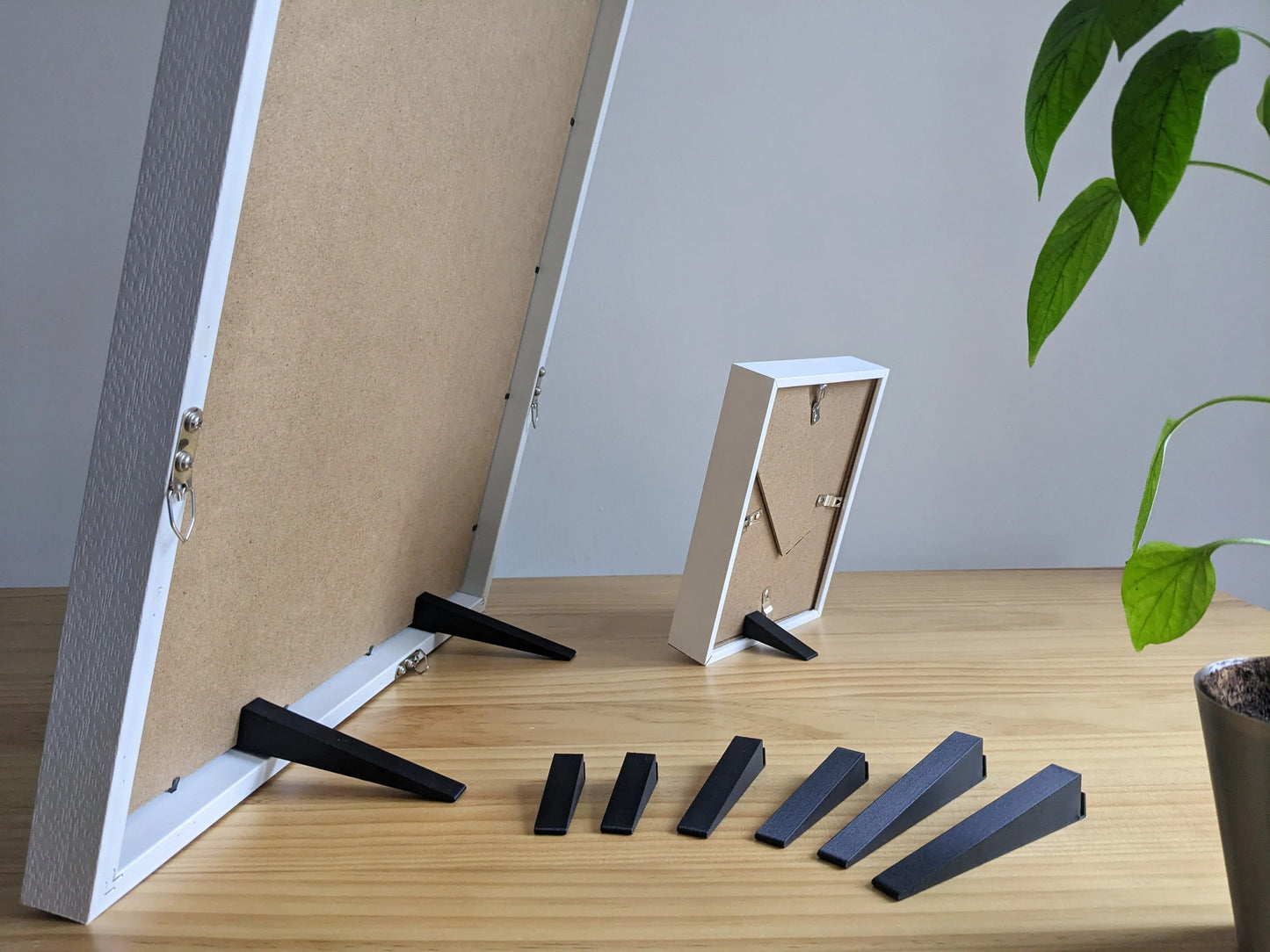 A selection of black picture frame stands displayed in front of a large frame that is being supported by a large picture frame stands, and a small picture frame being supported by a small picture frame stand.