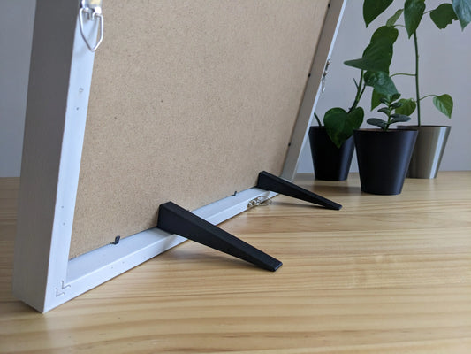 Two large picture frame stands attached to the back of a large picture frame stands, helping it to stand up.