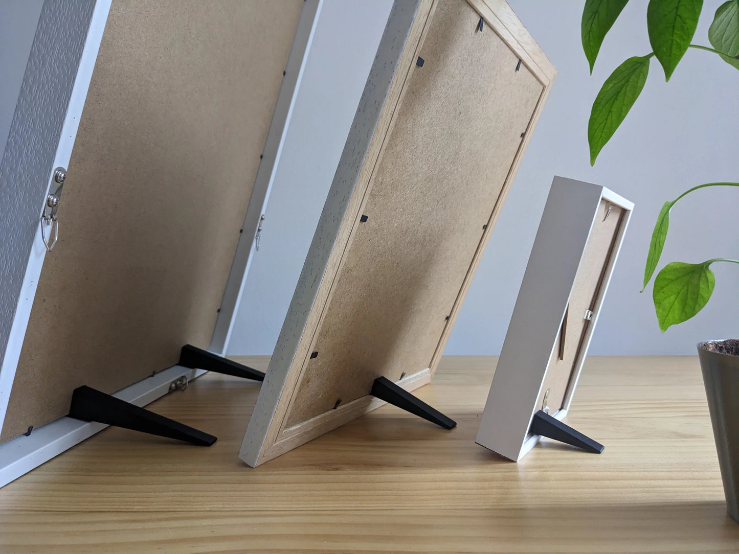 Three picture frames of different sizes being supported by small, medium and large picture frame stands.